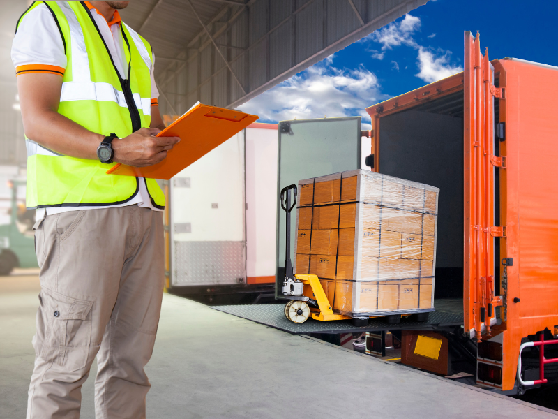 Worker with clipboard overseeing pallet loading onto a truck